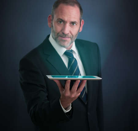 Mature businessman serving with tablet PC , looking into the cameraの写真素材