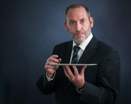 Mature businessman serving with tablet PC , looking into the cameraの写真素材