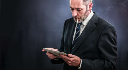 Mature businessman working with tablet PC , smoking a cigaretteの写真素材