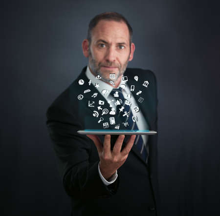 a mature businessman or salesman shows his pad with lots of apps flying aroundの写真素材