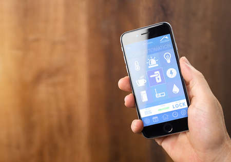 smarthouse home automation device with app icons. Man uses his smartphone with smart home security app to unlock the door of his house.の写真素材