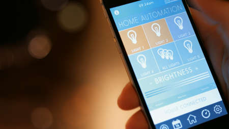 Smart House, home automation, device with app icons. Man uses his smartphone with smart home app to control the lights of his house.の写真素材