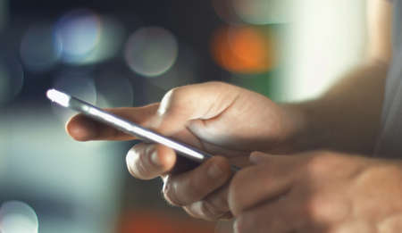 Business Man using mobile phone smart phone in the office. Typing, reading, scrolling the touchscreen - blurry background with space for text.の写真素材