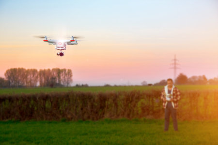 Modern RC UAV Drone quadro copter with camera flying on a clear sunny sky sunset background with...
