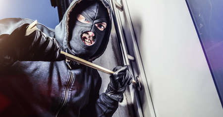 masked burglar with crowbar breaking and entering into a victim's home - shot with dramatic motionの写真素材