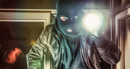Masked burglar with torch and crowbar breaking and entering into a house - shot with dramatic motionの写真素材