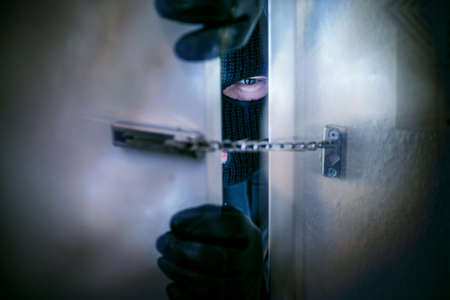masked burglar with crowbar breaking and entering into a victim's homeの写真素材
