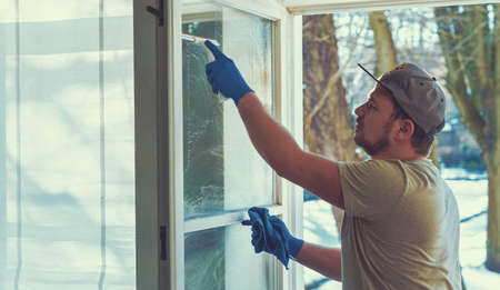 young man is using a rag and squeegee while cleaning windows. professional window cleaner.の写真素材