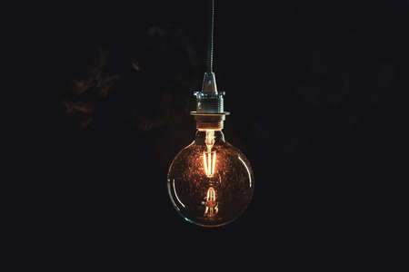 Vintage lightbulb on dark background with bright yellow shining wireの写真素材