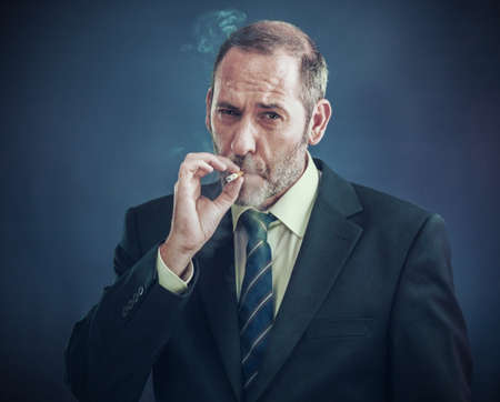Mature Businessman smoking a cigarette and looks into the cameraの写真素材