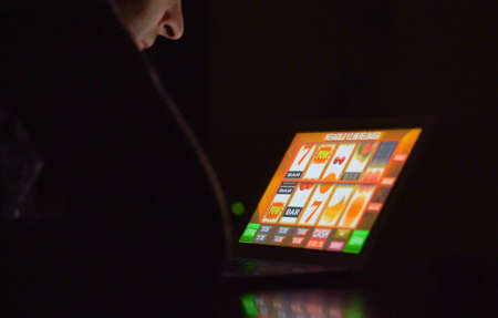 Gambling addicted man with glasses in front of online casino slot machine on laptop computer at night - loosing his money. Dramatic low light grain shot.の写真素材