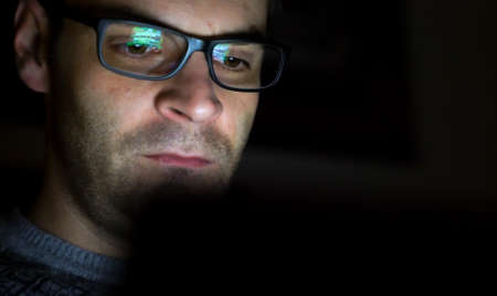 Gambling addicted man with glasses in front of online casino slot machine on laptop computer at night - loosing his money. Dramatic low light grain shot.の写真素材