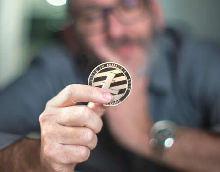 Litecoins - one Litecoin cryptocurrency in hand of a casual businessman wondering what the future isの写真素材