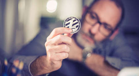 Litecoins - one Litecoin cryptocurrency in hand of a casual businessman wondering what the future isの写真素材
