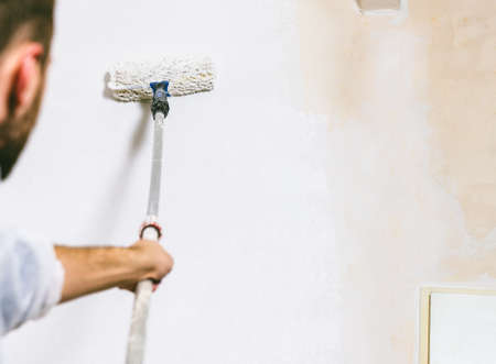 Close up of painter working with paint roller and brushes to paint the room in white colors. dig - do it yourselfの写真素材