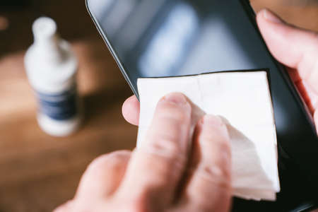 Person Cleaning mobile phone screen with disinfecting wipes for clean smartphone. COVID-19 Coronavirus outbreak contamination prevention concept.の写真素材
