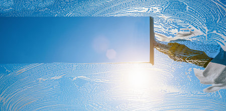 Window cleaner cleaning window with squeegee and wiper on a sunny day with a bright blue sky.
