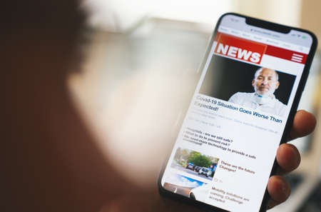 Online news on a smart phone. Close up of businessman reading news or articles in a mobile phone screen app. Hand holding smart device. Mockup website. Newspaper and portal on internet. Displayed news are not reality relatedの写真素材