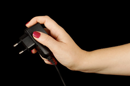 Female hand with mobile phone charger isolated on the black background