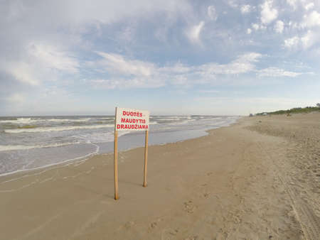 Sign of bathing prohibition in the empty Palanga beach. Text "Duobes. Maudytis draudziama" means bathing prohibition due to dabgerous wavesの写真素材