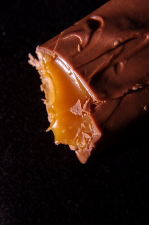 Bite off chocolate bar with tasty caramel macro close up isolated on the black background