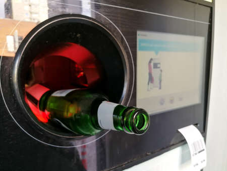 Green glass beer bottle close up inserted in the automatic reverse vending machine for recyclingの写真素材