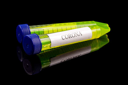 Yellow glowing liquids in the test tube with text CORONA isolated on the black reflective background. Corona COVID-19 virus concept.の写真素材