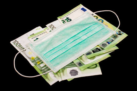 Face mask on top of many cash banknotes. Financial crisis caused by COVID virus conceptの写真素材