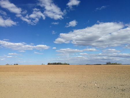 View of a plowed field below cloudy blue sky