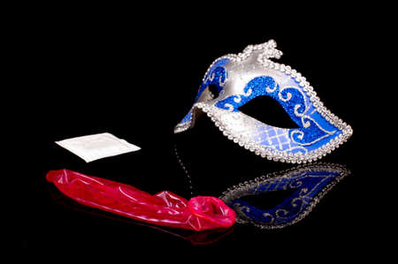 Sexy blue erotic face mask and pink used condom isolated on the black reflective backgroundの写真素材