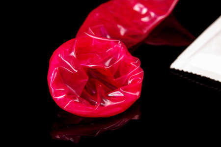 Used pink condom close up after sex isolated on the black reflective backgroundの写真素材