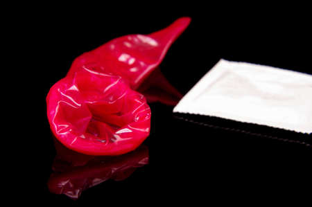 Used pink condom close up after sex isolated on the black reflective backgroundの写真素材