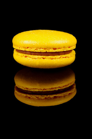 Colorful macaroon (macaron) cake macro close up isolated on the black reflective background. Traditional french dessertの写真素材
