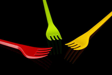 Three plastic disposable utensil cutlery forks yellow, green and red (Lithuania flag colors) isolated on the black backgroundの写真素材