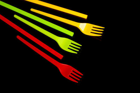 Plastic disposable utensil cutlery: yellow, green and red (Lithuania flag colors) forks and cocktail straws isolated on the black backgroundの写真素材