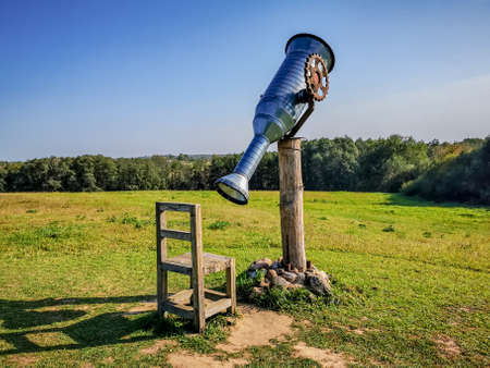 Giant sham telescope in the countryside and chair to wath itの写真素材