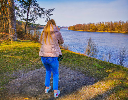 Girl in a park using binoculars in the park on the meadow to observe the panorama of the bend of the...