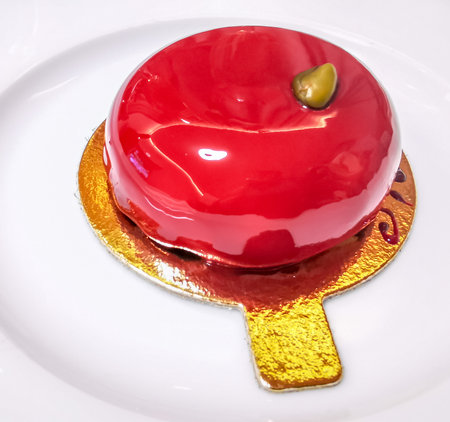 Pistachio flavored cake covered with a glossy fruity topping on a golden saucerの写真素材