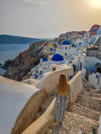 Girl with a dress watching a sunset in Oia village in Santorini, Greece. Picturesque view of traditional Santorini houses on the edge of the islandの写真素材
