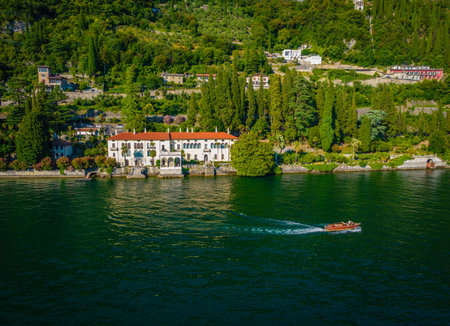 Aerial panoramic view of touristic villa Monastero located in Varenna resort, on the shore of lake Como, Italy with an old wooden speedboat passing byの写真素材