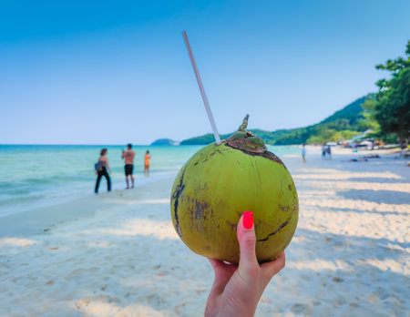 Coconut with straw in womans hand at a tropical white sand beach. Refreshing moment. Woman holding a coconut in her handsの写真素材