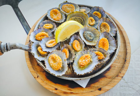 Grilled limpets served on a cast iron with a lemon slices in a restaurant in Azores island. Typical Atlantic ocean region seafood dishの写真素材