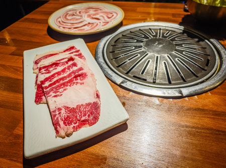 Korean BBQ style restaurant. Traditional Korea dining table with grill inside. Pork belly and beef ready to grill on charcoal stoveの写真素材