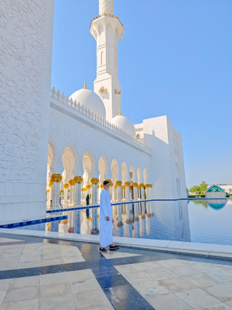 White man in traditional white Arabic abaya dress standing in front of Sheikh Zayed Grand Mosque in Abu Dhabi, United Arab Emiratesの写真素材