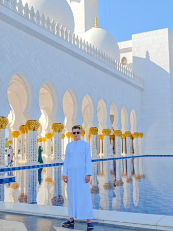 White man in traditional white Arabic abaya dress standing in front of Sheikh Zayed Grand Mosque in Abu Dhabi, United Arab Emiratesの写真素材