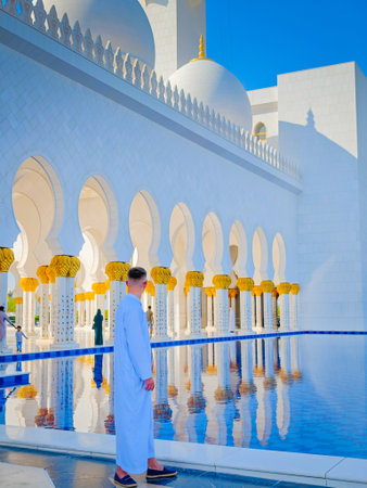 Man in traditional white Arabic abaya dress standing in front of Sheikh Zayed Grand Mosque in Abu Dhabi, United Arab Emiratesの写真素材