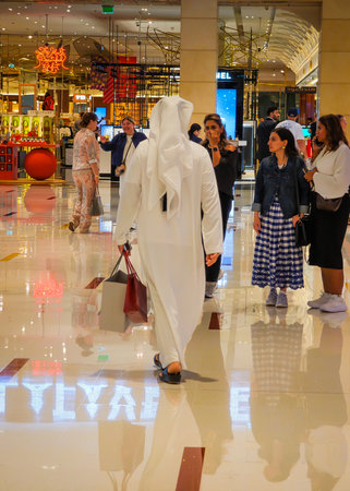 11 30 2025 - Dubai, United Arab Emirates. Back view of Emirati men walking dressed in kandura thawb with shopping bags inside Dubai Mallのeditorial素材