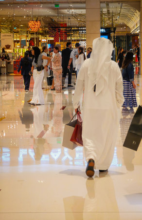 11 30 2025 - Dubai, United Arab Emirates. Back view of Emirati men walking dressed in kandura thawb with shopping bags inside Dubai Mallのeditorial素材