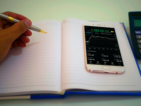 Business man using a mobile phone device with stock graph,checking market dataの写真素材