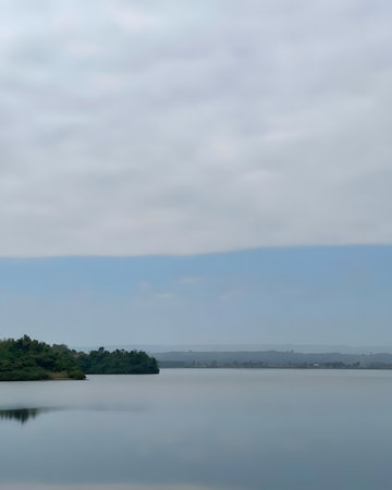 Minimalist landscape of a calm lake and tree-covered shore with smooth water reflection and open sky, offering clean copy space for creative projects.の写真素材